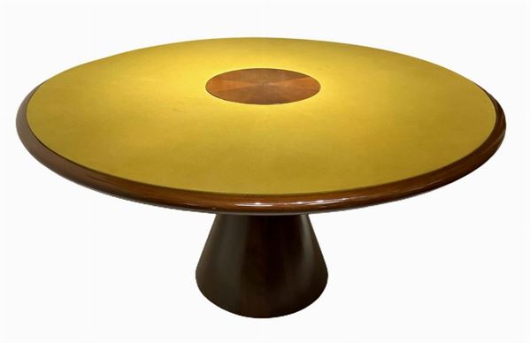Produzione italiana nello stile di Angelo Mangiarotti. Importante tavolo con struttura in legno impiallacciata noce e finitura lucida. Piede tronco conico e piano rotondo rivestito in panno nei toni del senape. Segni di uso. Anni 70. D 135 cm, h 70 cm
