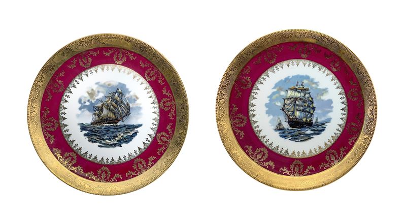 Coppia di piatti in porcellana bordeaux e oro con un galeone al centro
