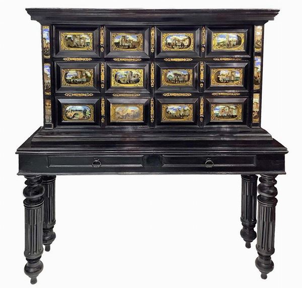 Monetiere in legno nero ebanizzato a due corpi, XVIII secolo. 12 formelle ai cassetti con pitture su vetro raffiguranti paesaggi con architetture. Avente come base tavolo in legno ebanizzato. H Cm 162. Cm 150x45
