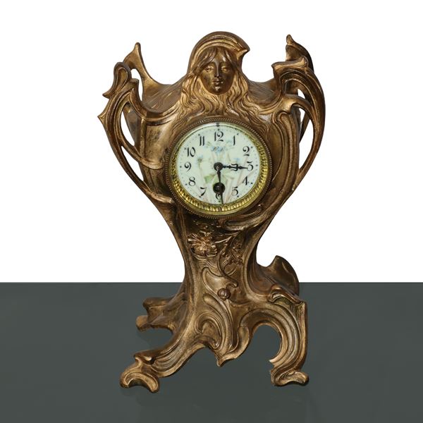 Floral art nuveau table clock in golden metal, enamelled porcelain dial with female figure in relief on the cymatium