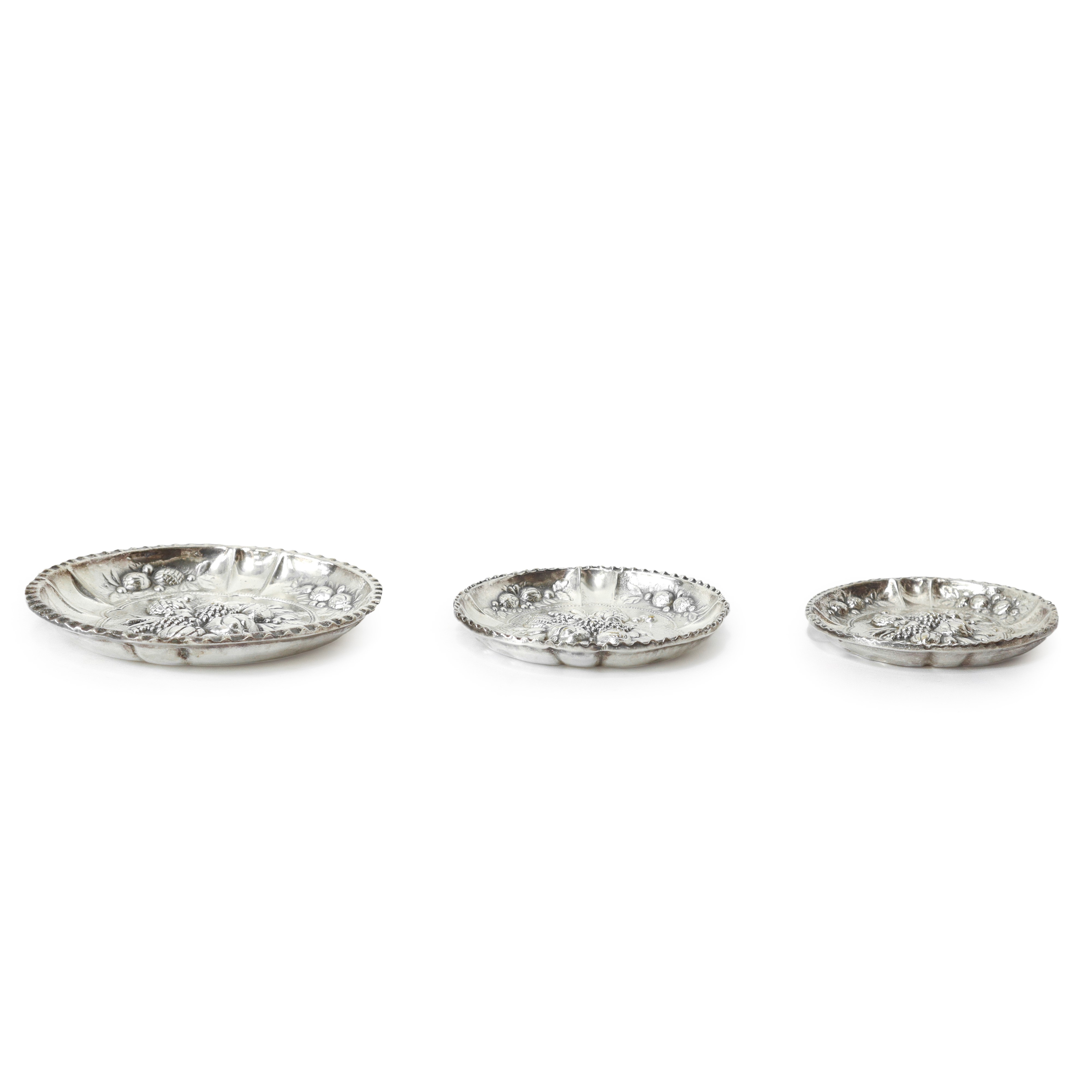 Tris di piattini in silver con decorazioni di frutti a sbalzo in argento, diametri 9,6 - 11,3 - 1...
