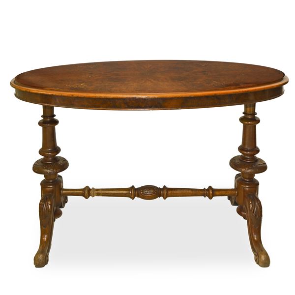 Oval table in walnut root, top inlaid in light wood, feet with central tie carved in acanthus leaf