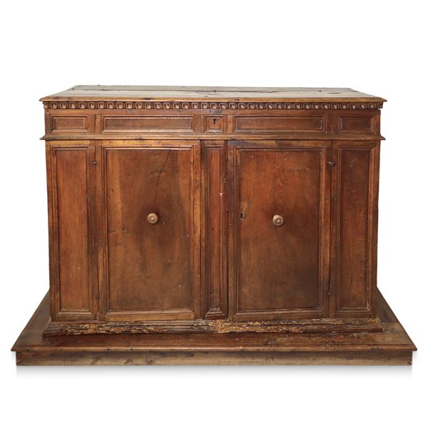 Grande credenza bassa in legno di noce, piano a becco di civetta sottolineato da  dentellatura intagliata, due ante con gangheri cornice alla base