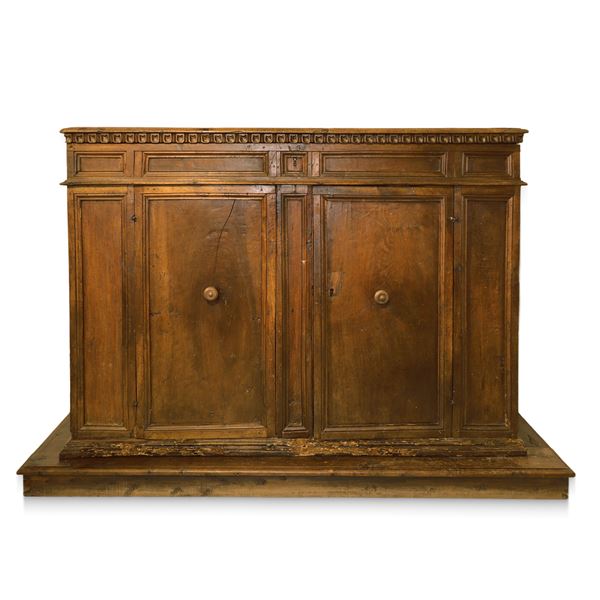 Grande credenza bassa in legno di noce, piano a becco di civetta sottolineato da  dentellatura intagliata, due ante con gangheri cornice alla base
