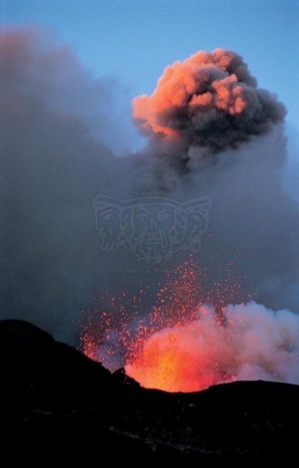 Collezione EM, titolo "Montagnola", anno 2001. Etna: eruzione 2001, esplosione di lava alla base della Montagnola, sullo sfondo fumo dal cratere colorato dalla luce del tramonto, diapositiva  1 / 8 , 30x45, CIBACHROME stampa diretta da diapositiva , 40x55 forex 10mm, perfilo bianco, cartoncino, bordi rivestimento sabbia vulcanica 