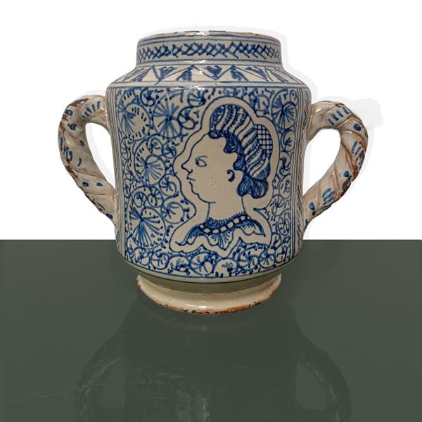 Ceramic pharmacy jar with blue decorations on a white background and profile face, two handles