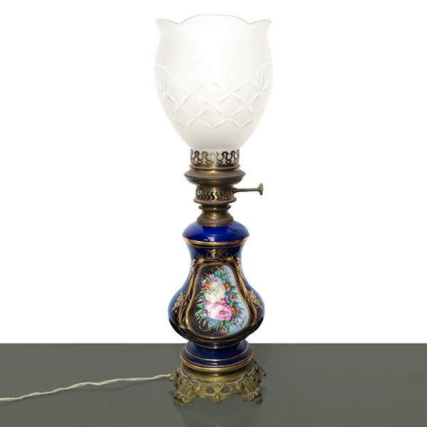 Blue porcelain lamp with polychrome flowers painted on the front within a golden oval with a carved glass diffuser