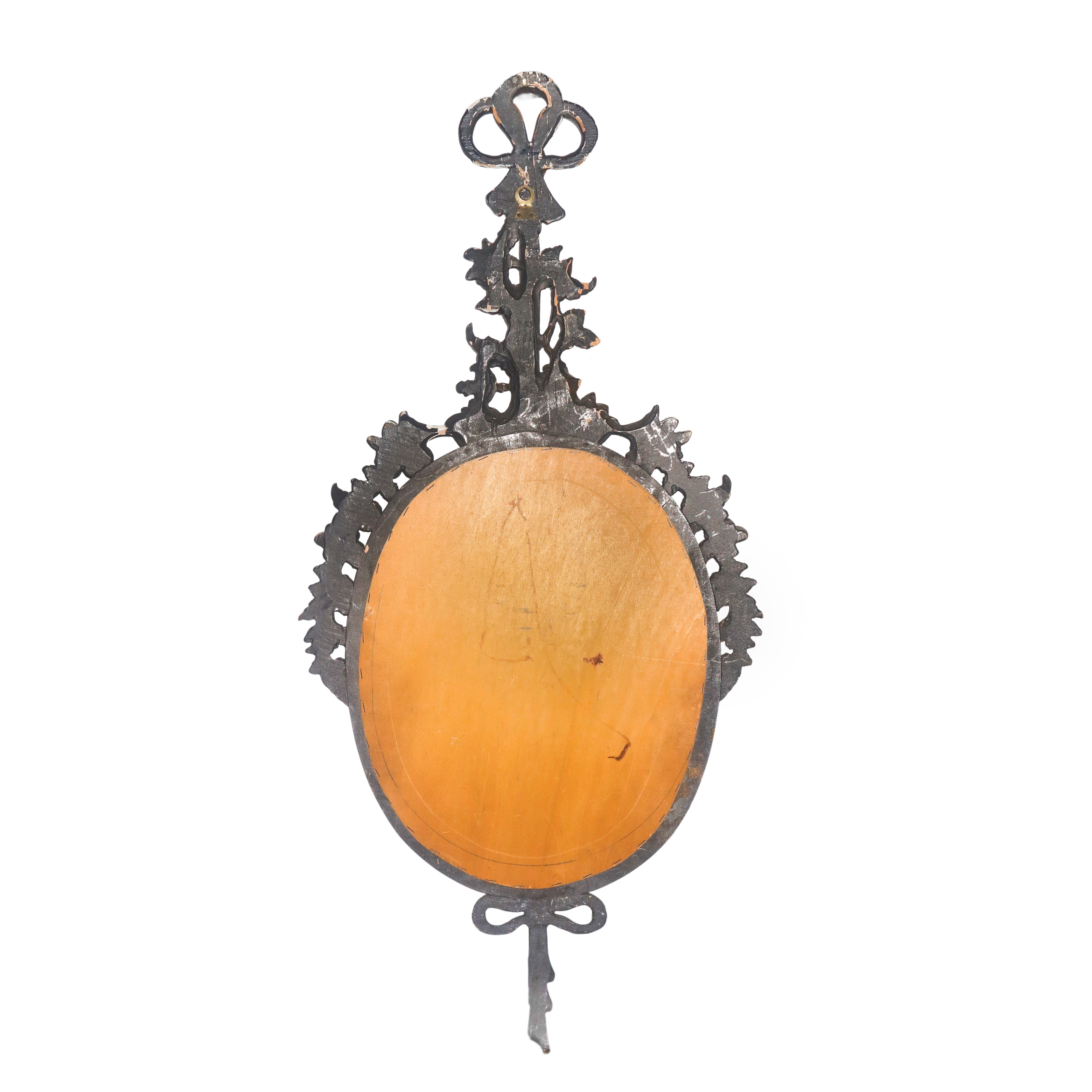 Specchiera ovale entro cornice dorata con decori floreali e fiocchi pendenti alla sommità e alla ...