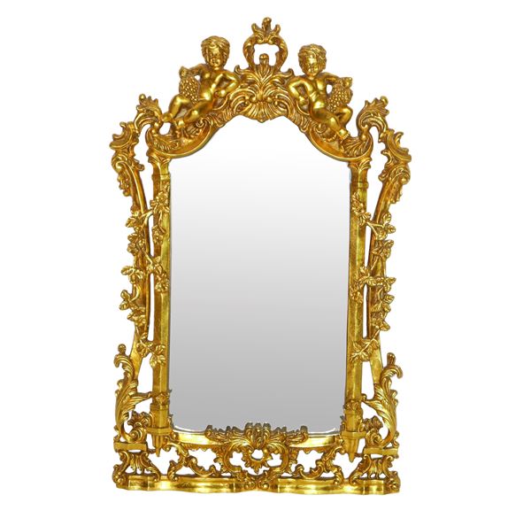 Specchiera sagomata entro cornice dorata riccamente decorata a traforo con due bacchini alla sommità
