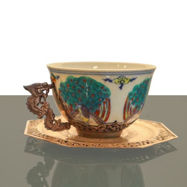 Chinese porcelain tea cup painted in polychrome with metal handle in the shape of a dragon and metal saucer with filigree edges