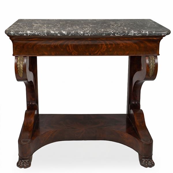 Consolle Carlo X in legno scolpito con lastronatura in piuma di mogano arricchita da bronzi cesellati e dorati. Piano in marmo grigio stondato in testa