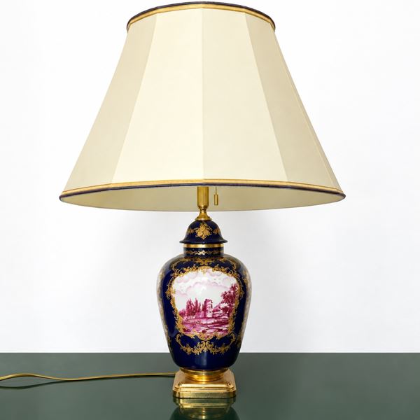 Blue porcelain table lamp with a medallion on the front with a landscape painted in shades of burgundy and a medallion on the back with a floral decoration painted in shades of burgundy
