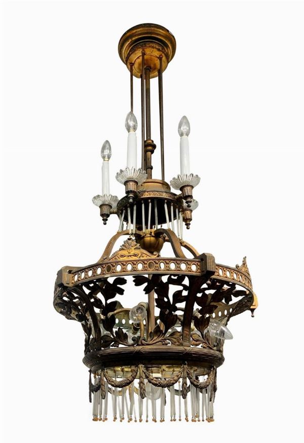 Lampadario in ottone dorato, inizi XX secolo. Cannule in vetro e decorazione in ottone nei modi dello stile liberty, a 11 luci.
H 110 cm, Diametro ... 