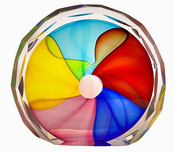 Scultura in vetro pesante di forma circolare con inclusioni di pasta vitrea policroma. Superficie riportante molature lucide.
H cm 22x26