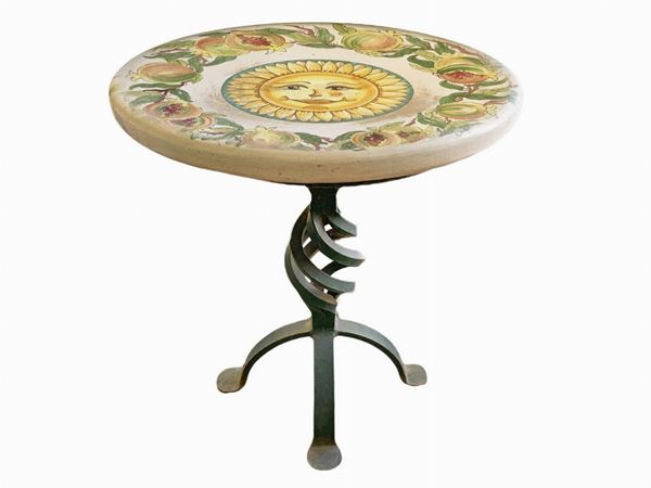 Tavolo basso in pietra lavica decorato a ceramica policroma con sole centrale. XX secolo,H cm 47, diametro cm 40. Struttura portante in ferro battuto.