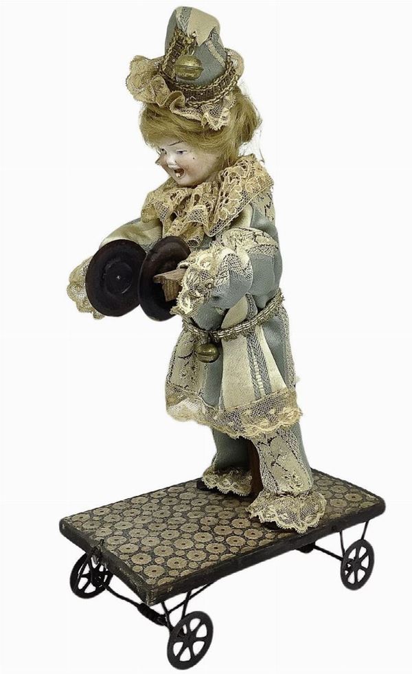 Giocattolo antico con clown musicante, fine XX secolo. Testa, piedi e mani in legno, vestiti in tessuto. Funzionamento a spinta, dotato di ruote. H cm 33 x17