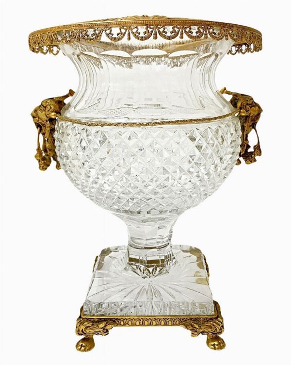 Vaso in cristallo molato con ottoni dorati. Base quadrata con piedi leonini. XX secolo,Inizi XX secolo. Borchie di teste di leone ai lati. H cm 34. H ... 
