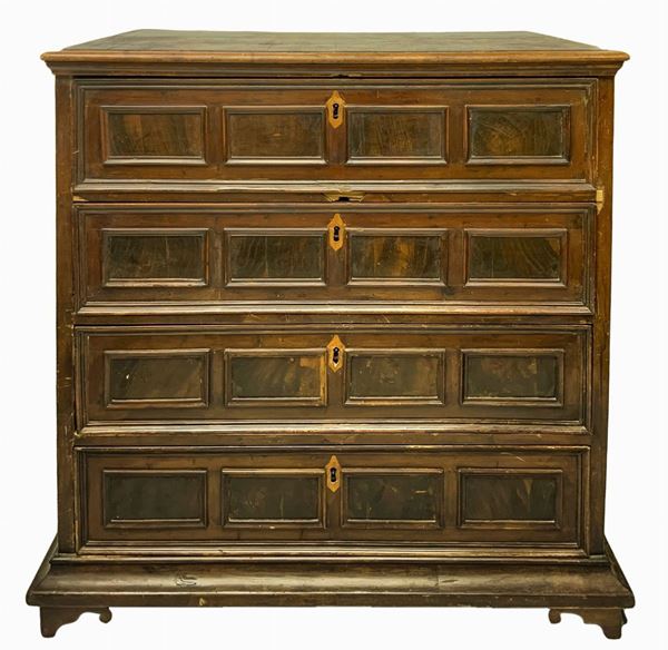 Cassettone in legno di noce, fine XVII secolo, Emilia. Sul fronte quattro cassetti decorati ciascuno con formelle lastronate in palissandro. Sui laterali grandi formelle entro cornici rettangolari. Piedi a mensola. H cm 125x105x60