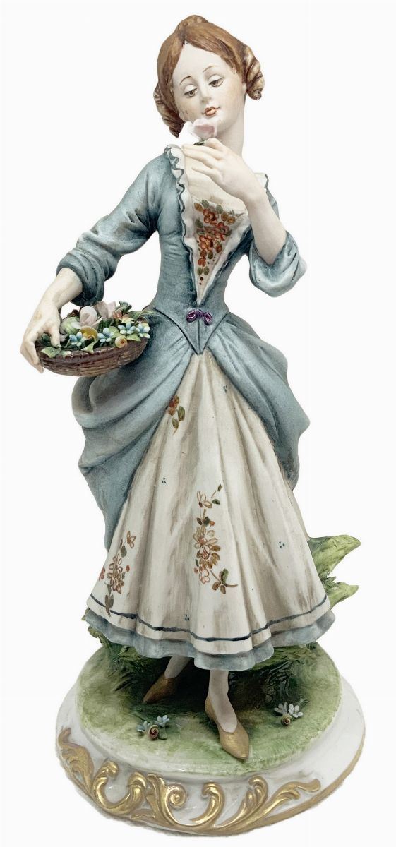 Statuetta in porcellana di Capodimonte raffigurante dama con cesto di fiori. 
H cm 26. 